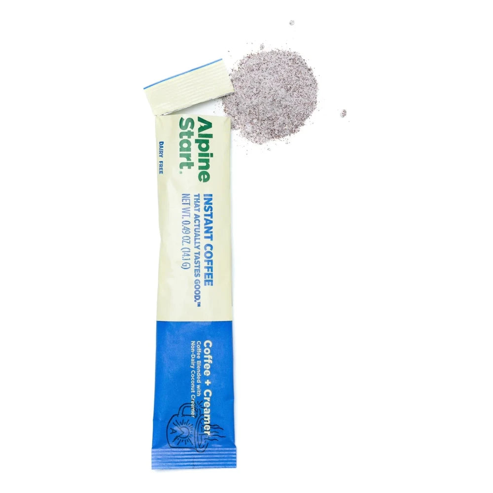 Alpine Start Coffee + Creamer single cream and blue stick packet open and tilted with loose coffee-creamer powder spilling out on white background, showing Dairy Free and Coffee Blended with Non-Dairy Coconut Creamer branding