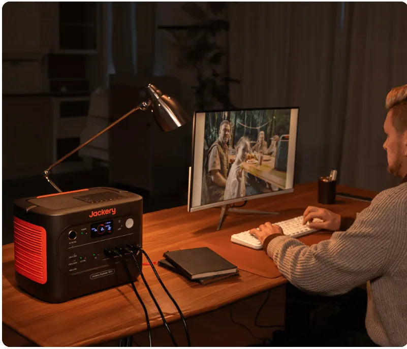 Jackery 1500 V2 power station powering home office desk setup with monitor and lighting.