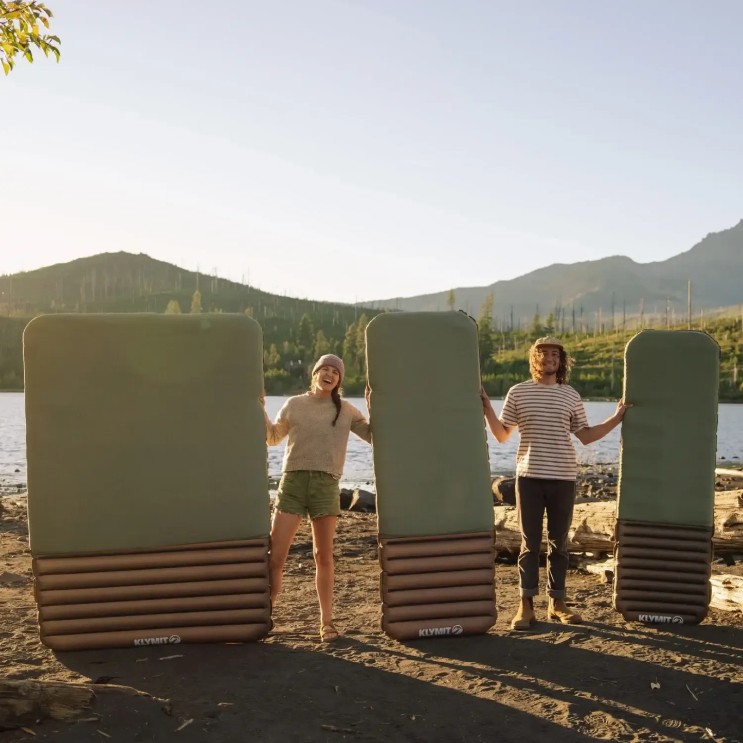 Campers holding Klymit Klymaloft Summit sleeping pads by a lake showcasing size and outdoor use