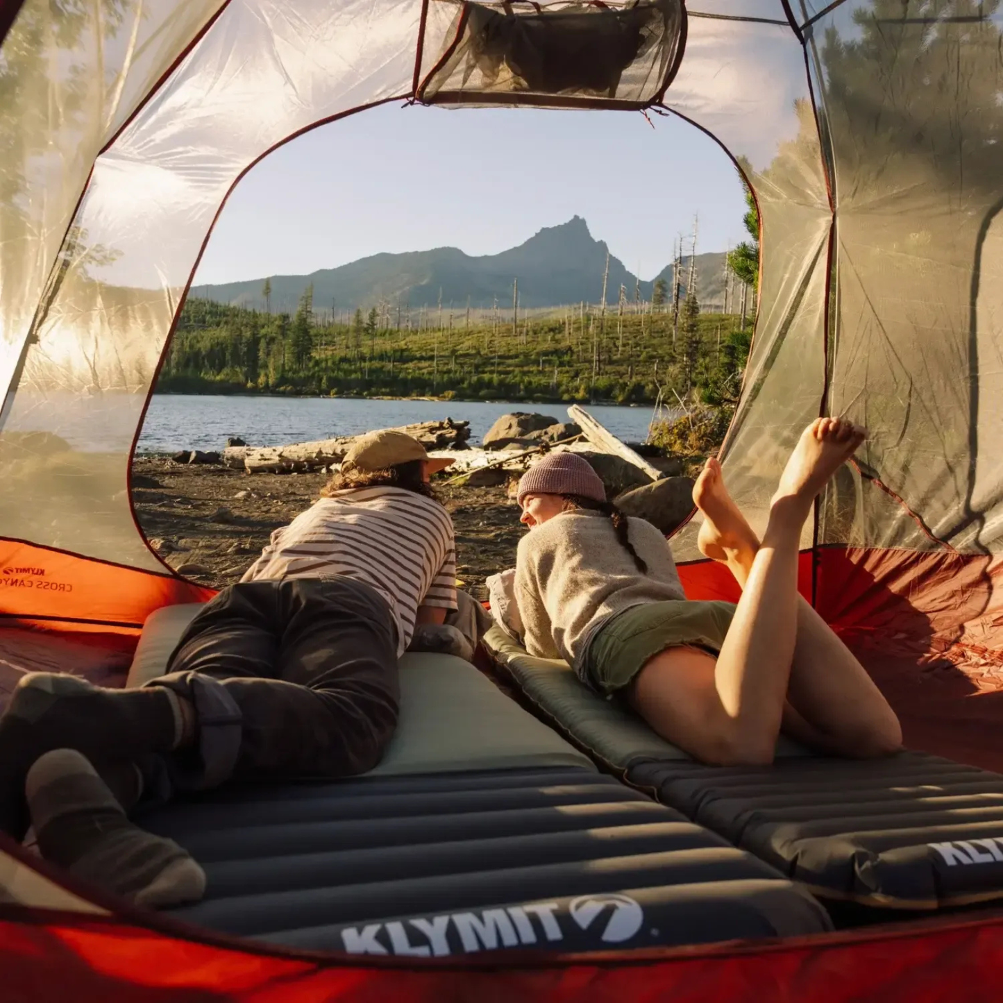 Couple relaxing on Klymit sleeping pads inside tent with mountain lake view