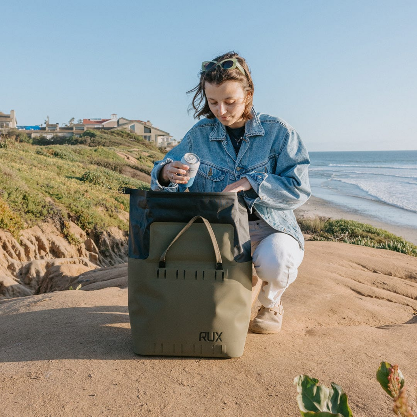Rux 25L soft cooler bag in use at the beach with person placing a drink inside.
