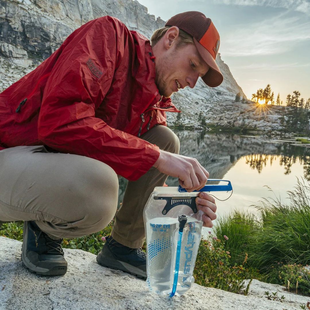hiker filling platypus big zip evo reservoir with water at alpine lake during sunset