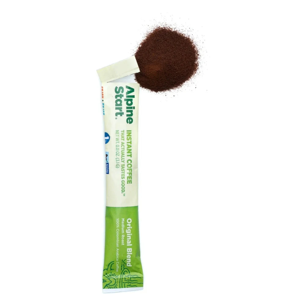 Alpine Start Original Blend instant coffee single stick packet open and tilted with loose coffee grounds pouring out on white background, showing green and white packaging with Original Blend branding