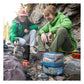 Man and woman cooking at rocky alpine campsite with BVONE collapsible bear canisters in the foreground filled with food, showing real-world backpacking camp use in mountain terrain
