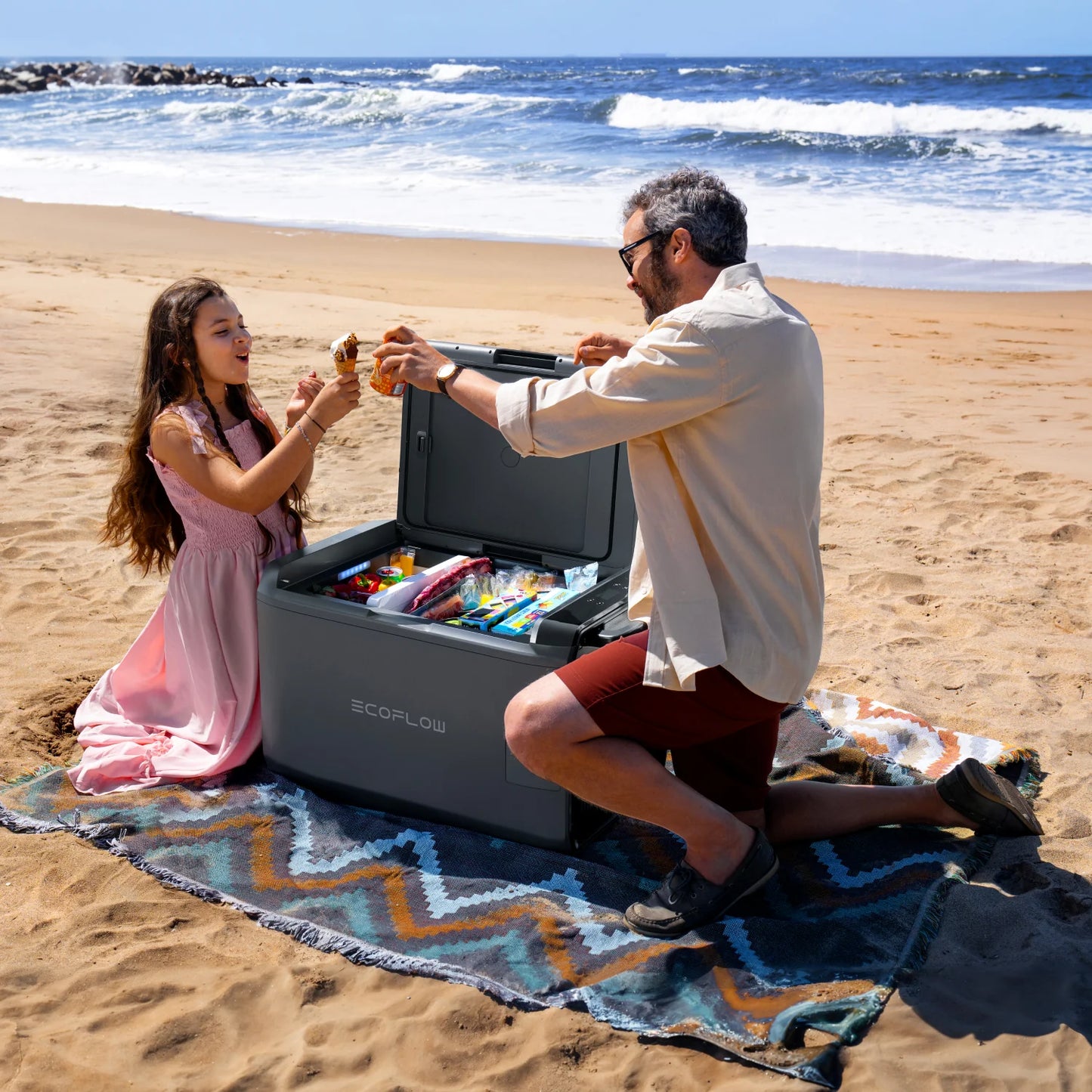 Family using an EcoFlow Glacier Classic cooler on a sandy beach with the lid open and food inside