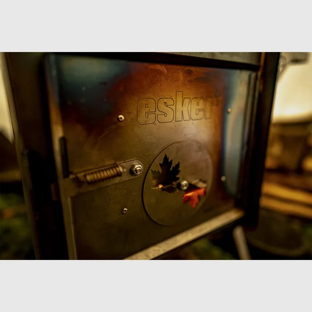 Close-up of the Esker Baffin wood stove door showing the Esker logo and maple leaf damper cut-out
