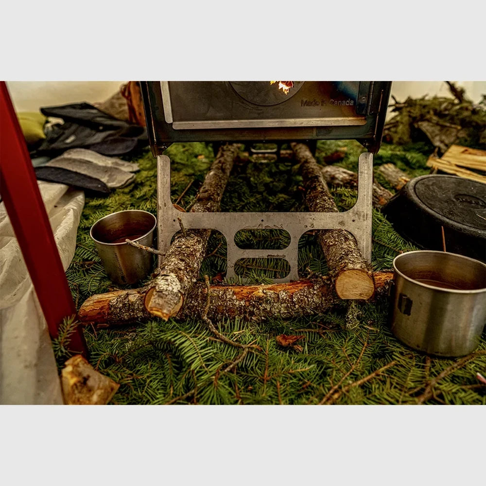 Esker Baffin wood stove set up with stovepipe and stacked firewood for winter hot tent camping