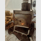 Close-up of the Esker Baffin stove's Snow Float legs stabilized on logs inside a winter hot tent