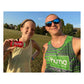 Enthusiastic female athlete wearing a green H√ºma Powered by Nature cap and white sports top laughing with multiple red Huma Chia Energy Gel Strawberry packets taped to her torso and arms, indoor lifestyle setting