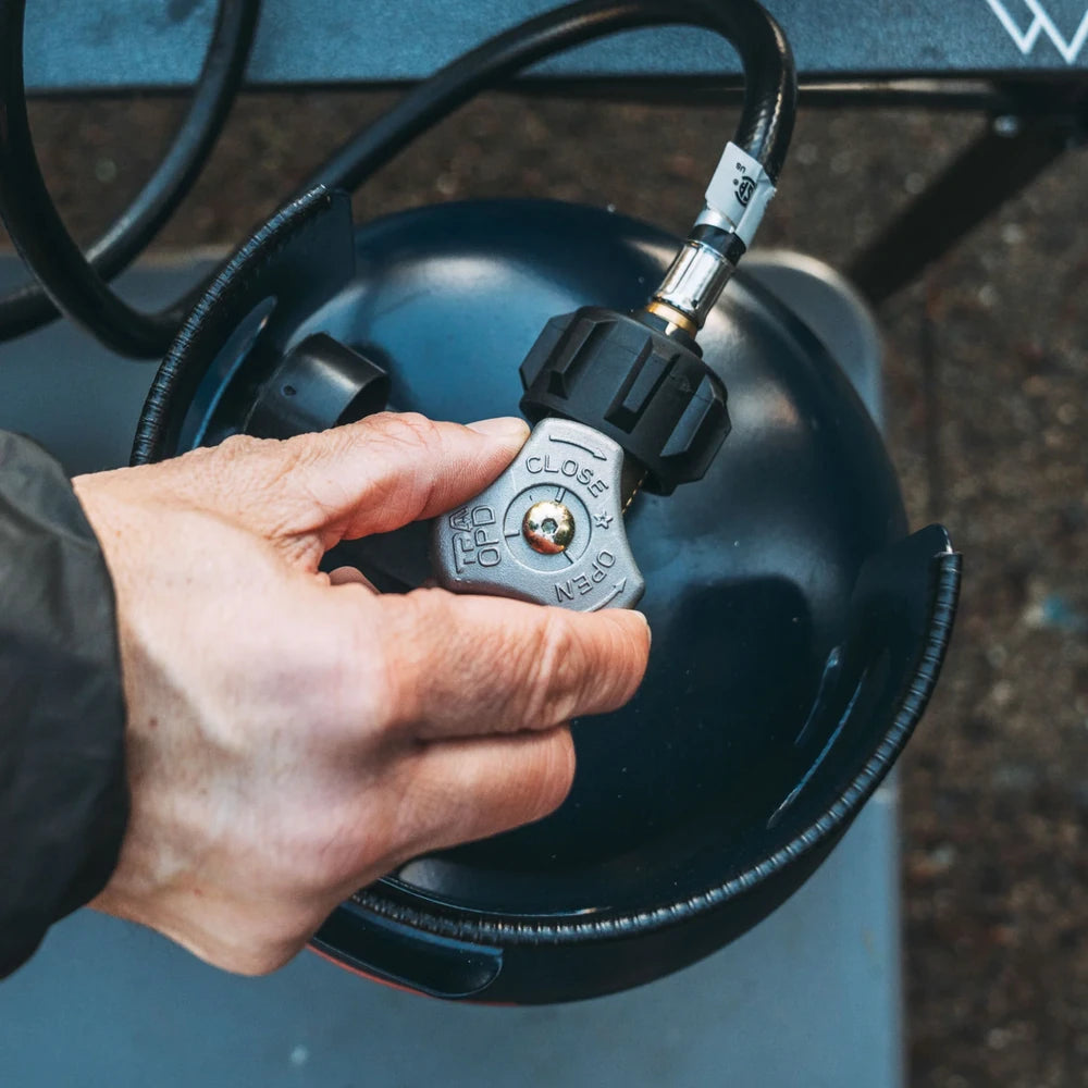 Hand turning the valve on an Ignik Gas Growler 3.8 lb refillable propane tank connected to a propane hose regulator
