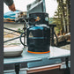Ignik Propane Growler Tank connected to a camp stove on an outdoor camp kitchen table beside a river