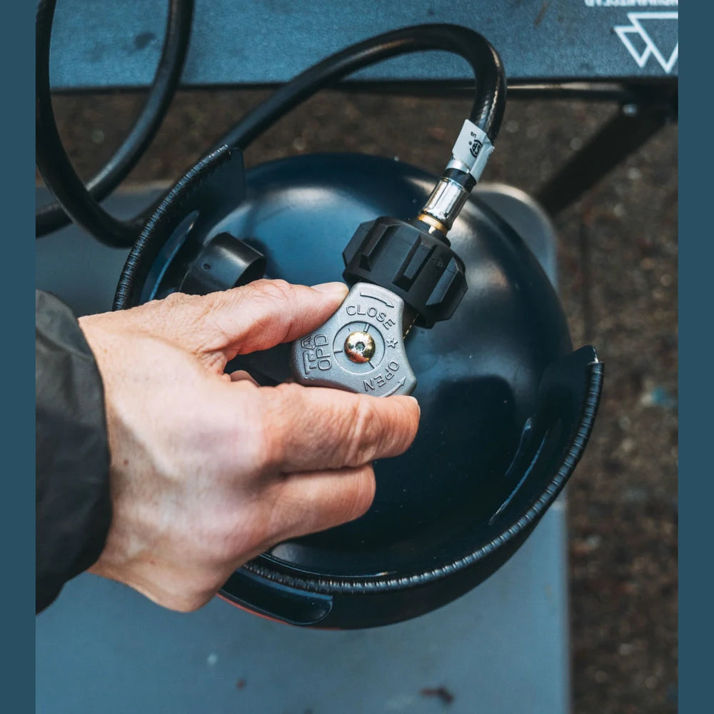 Hand turning the valve on an Ignik Propane Growler Tank showing the propane connection and regulator