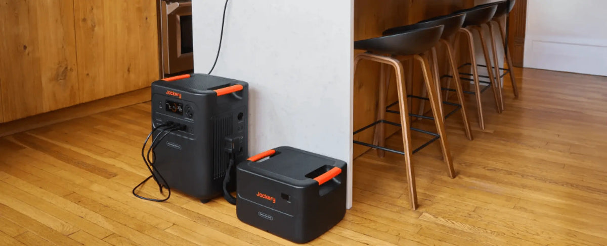 Jackery power station and expansion battery pack on a hardwood kitchen floor beside a counter with bar stools