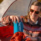 Camper holding packed Klymit Static V Base sleeping pad next to tent outdoors