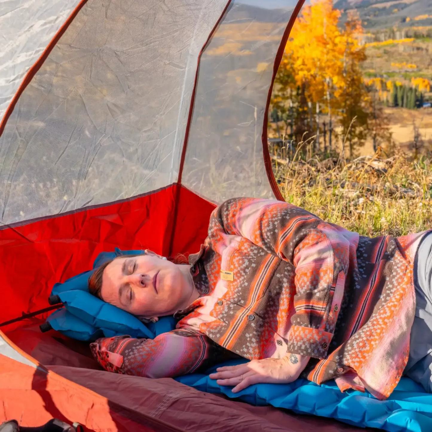 Person resting on Klymit Static V Base sleeping pad inside tent outdoors