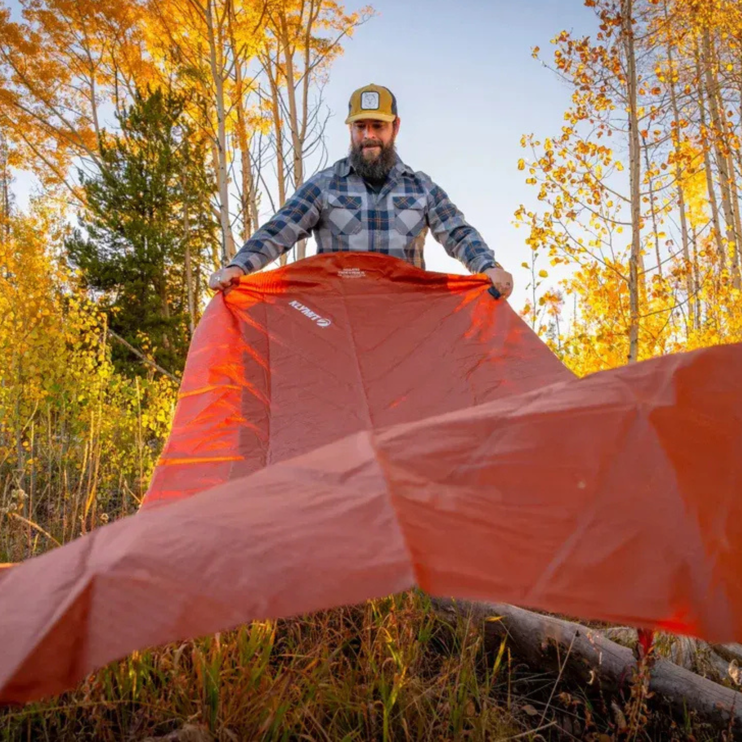 Man unrolling Klymit insulated sleeping pad outdoors in forest setting for camping and backpacking