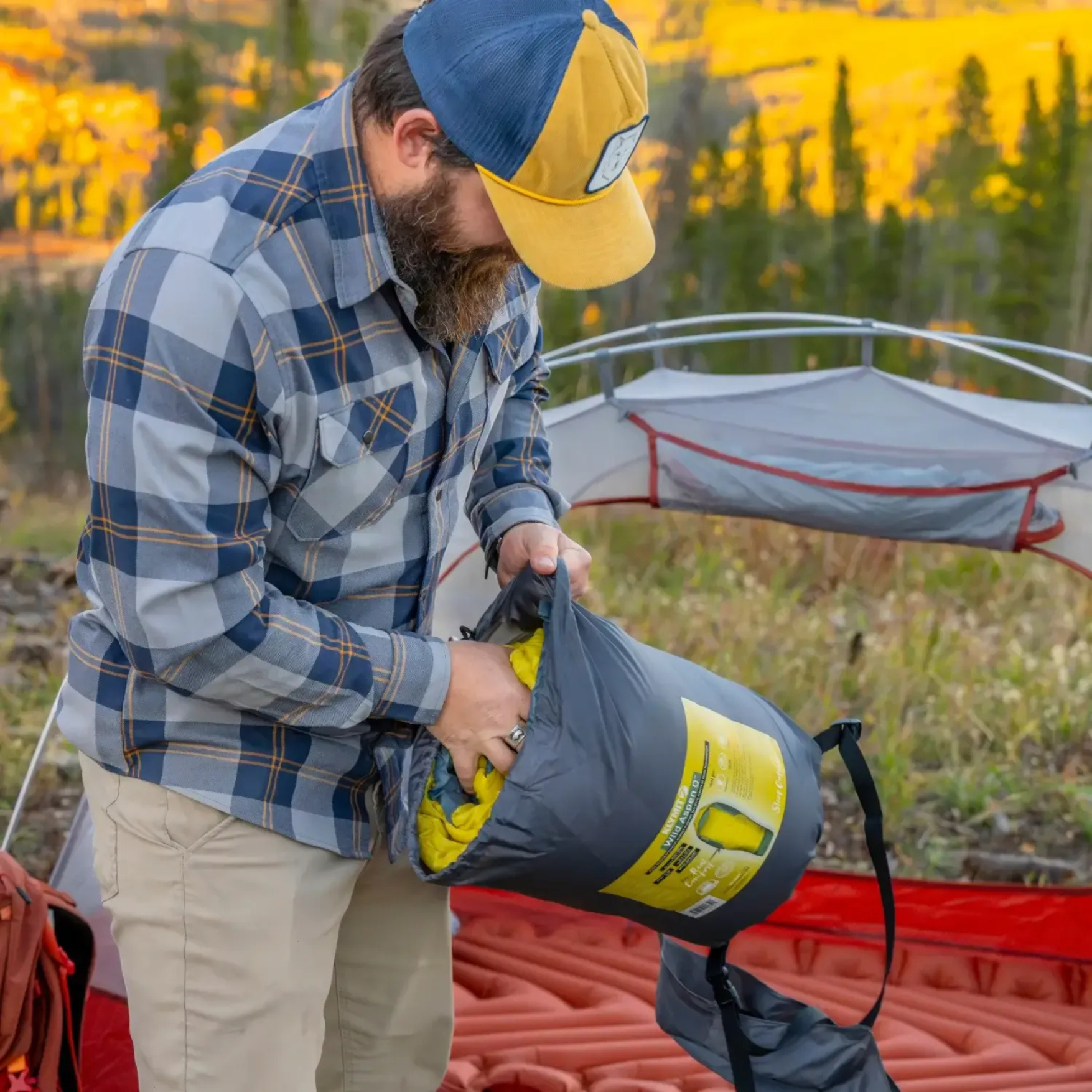 Camper packing Klymit Wild Aspen 0 sleeping bag into compression sack at campsite