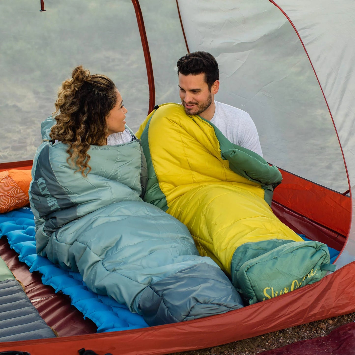couple using Klymit Wild Aspen 20 sleeping bags inside tent camping outdoors