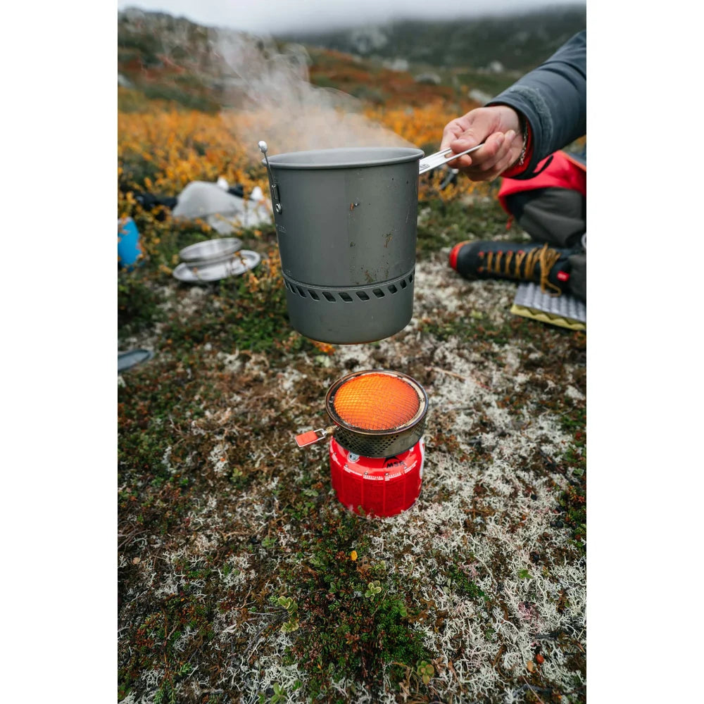 Backpacker lifting MSR Reactor stove pot off glowing radiant burner at Norway tundra plateau campsite, showing fast-boil all-weather cooking performance