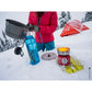 Woman pouring boiled water from MSR Reactor stove pot into water bottle in snowy winter camp, glowing radiant burner and red MSR tent visible in background