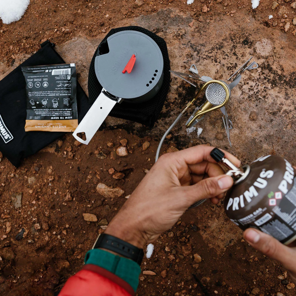 Primus gas canister powering backpacking stove while boiling water outdoors in cold weather