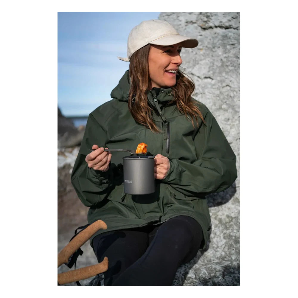 Person eating from Primus Trek Pot UL with Primus Trekking Spork at coastal hiking campsite with rocky shoreline and ocean in background