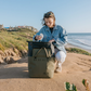 Rux 25L soft cooler bag in use at the beach with person placing a drink inside.