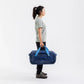 Side profile of a woman carrying the navy Sea to Summit Meridian Duffle Bag by its light blue top handles
