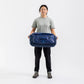 Woman holding a navy Sea to Summit Meridian Duffle Bag in front of her to show its size