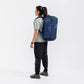 Rear view of a woman wearing the navy Sea to Summit Meridian Duffle Bag as a backpack with shoulder and waist straps