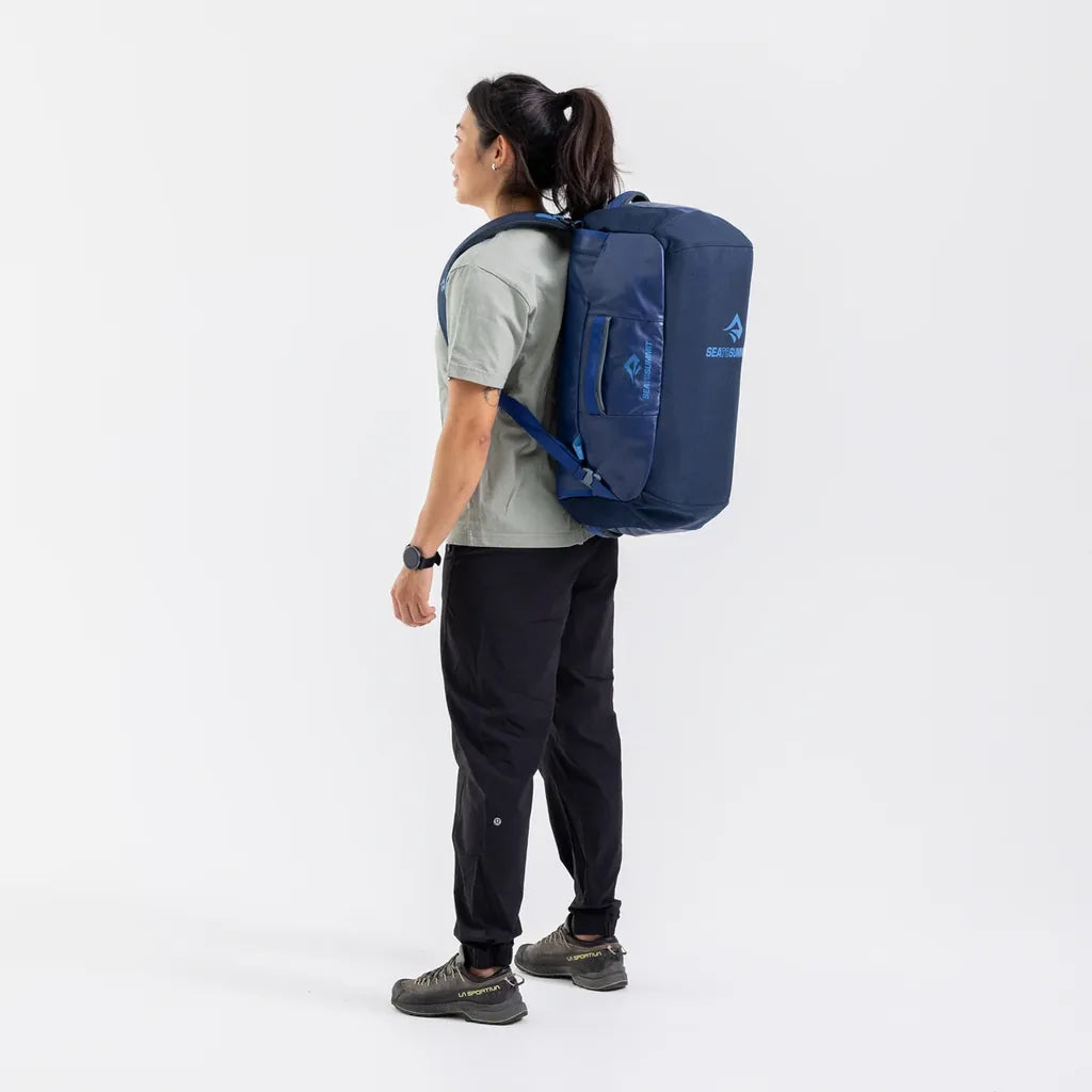 Rear view of a woman wearing the navy Sea to Summit Meridian Duffle Bag as a backpack with shoulder and waist straps