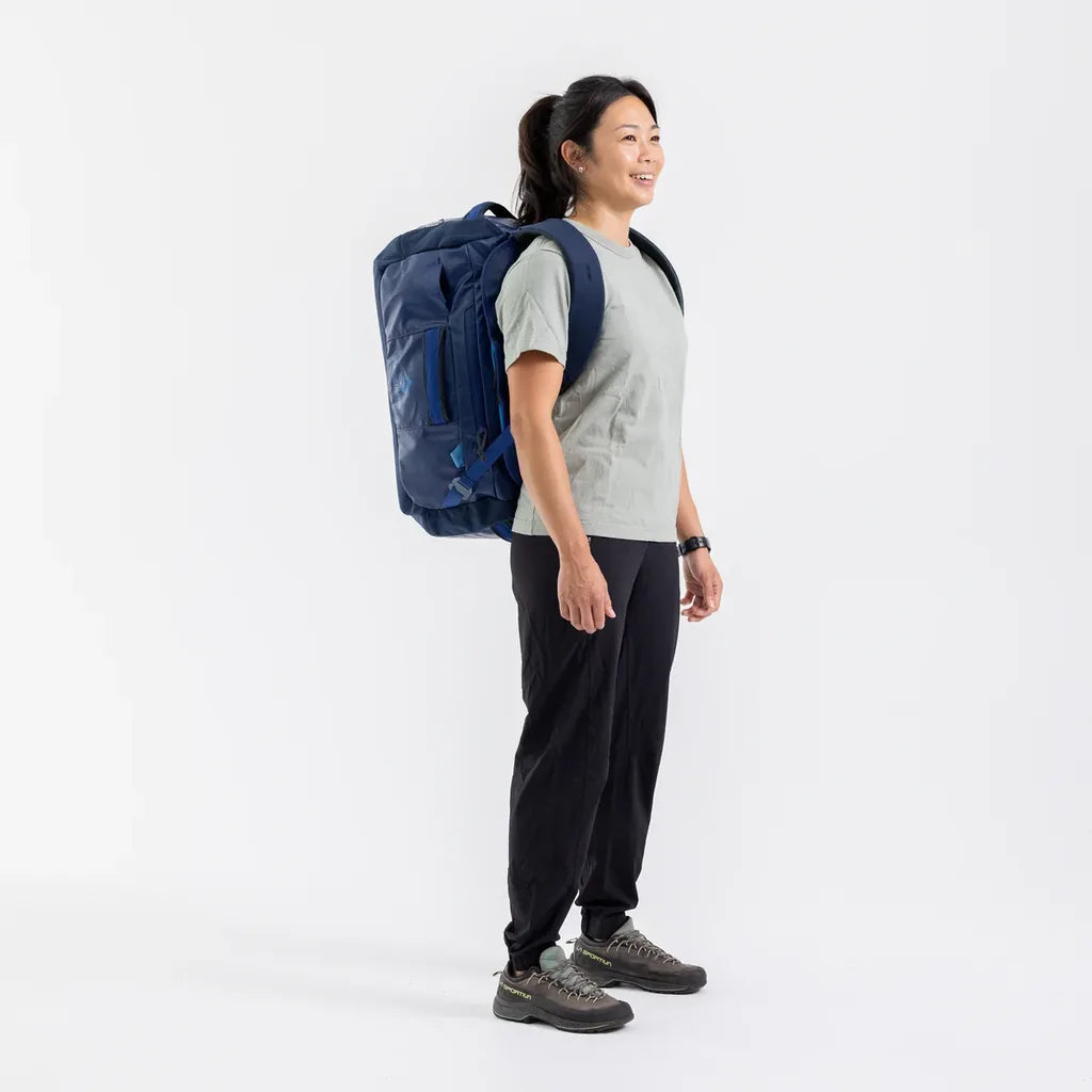 Woman smiling while wearing the navy Sea to Summit Meridian Duffle Bag as a backpack, three-quarter view