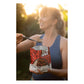 Sly Foods General Tao meal lifestyle shot outdoors showing a smiling woman in a blue tank top eating from a black spork while holding the open red SLY General Tao package, backlit by warm golden hour sunlight with soft green foliage in the background