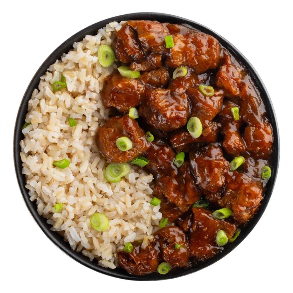 Sly Foods General Tao prepared meal top-down view on white background showing a black bowl filled with glazed plant-based protein pieces in rich brown sauce alongside brown rice, garnished with sliced green onions