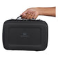 Stanley All Day Midi Lunch Box 6.3QT in Black handle close-up detail on white background showing a hand gripping the molded black top carry handle with silver metal zipper pull hardware, and Stanley winged bear logo embossed on the black textured hard-shell body below