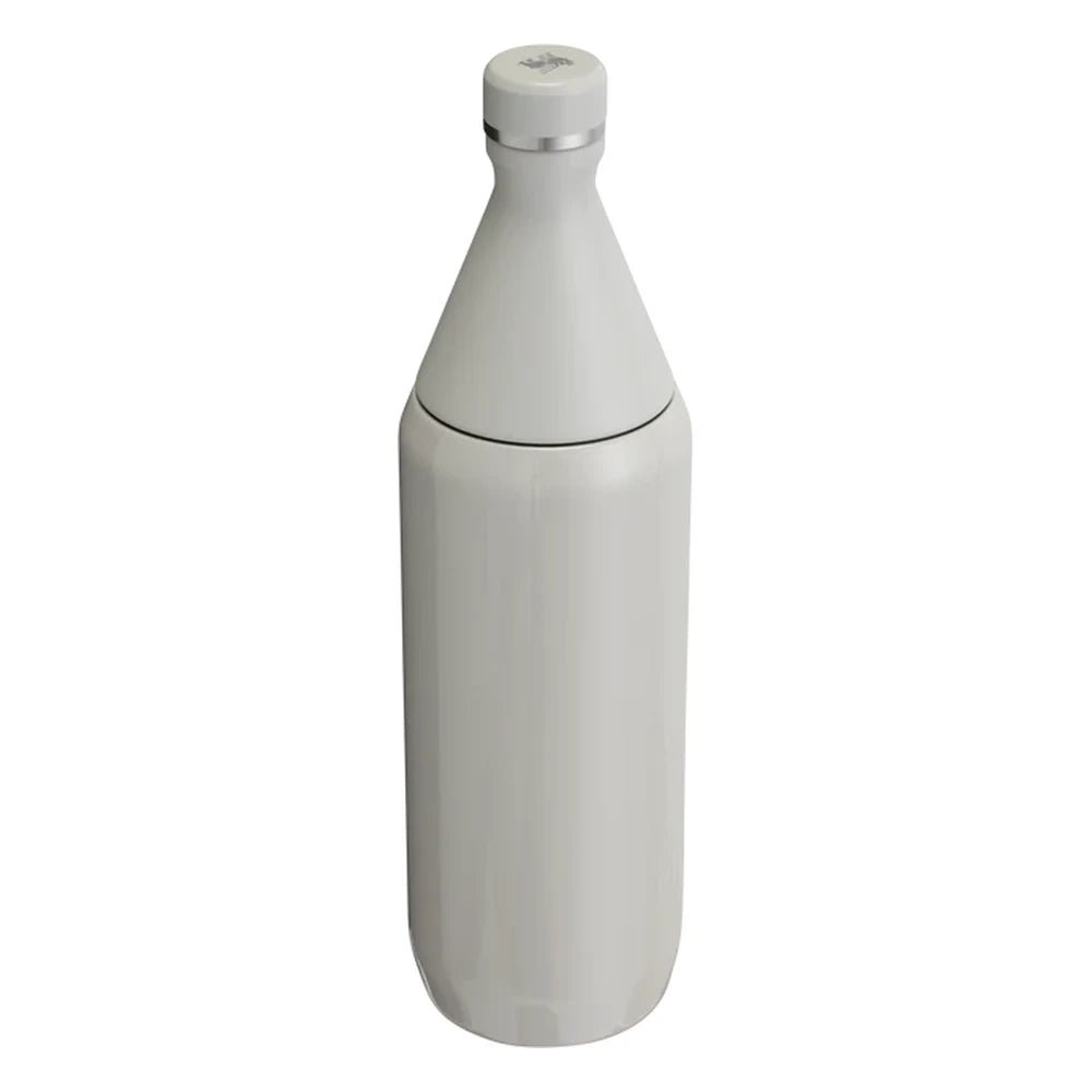 Stanley All Day Slim Bottle 34oz in Ash Gloss back view on white background showing smooth warm gray gloss cylindrical body, tapered cone neck, flat cap with Stanley bear icon on top, and stainless steel trim ring at the neck
