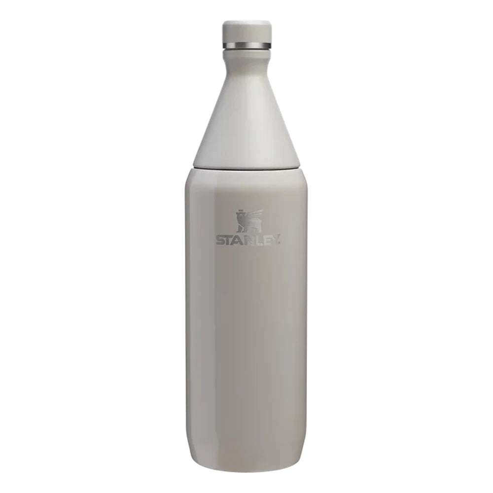 Stanley All Day Slim Bottle 34oz in Ash Gloss front hero on white background showing warm gray gloss tapered slim bottle with cone-shaped neck, flat screw cap with Stanley winged bear icon, engraved Stanley winged bear logo on body, and stainless steel trim ring at the neck