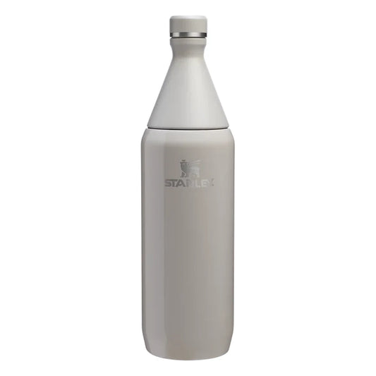 Stanley All Day Slim Bottle 34oz in Ash Gloss front hero on white background showing warm gray gloss tapered slim bottle with cone-shaped neck, flat screw cap with Stanley winged bear icon, engraved Stanley winged bear logo on body, and stainless steel trim ring at the neck