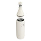 Stanley All Day Slim Bottle 34oz in Cream Gloss exploded view on white background showing all components separated: flat cap with Stanley bear icon floating above, the cone-shaped upper neck section with black sealing gasket and stainless steel threaded opening, and the cylindrical lower body with open stainless steel interior and Stanley logo