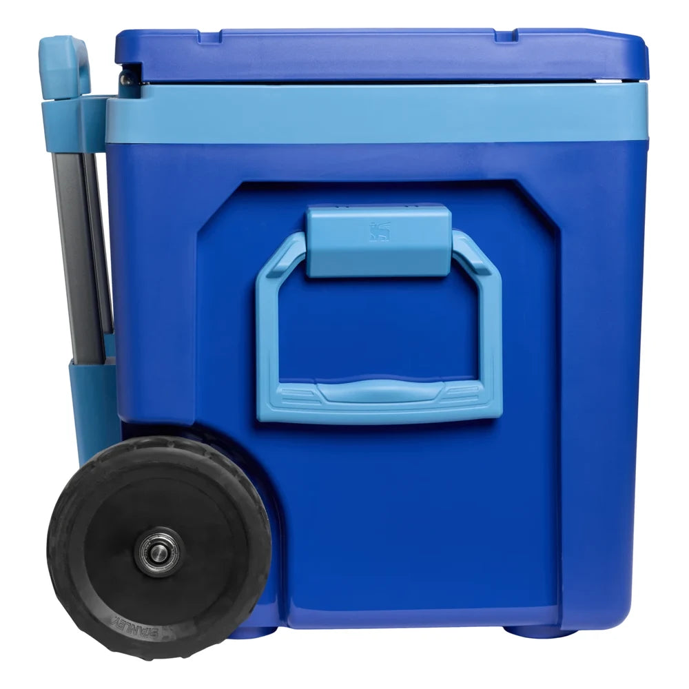Stanley The Cold For Days Wheeled Outdoor Cooler 50QT in Azure Blue side view on white background showing the sky blue side carry handle with Stanley bear icon and locking release, cobalt blue body, sky blue lid trim, and large black all-terrain wheel with Stanley-branded tread at the base
