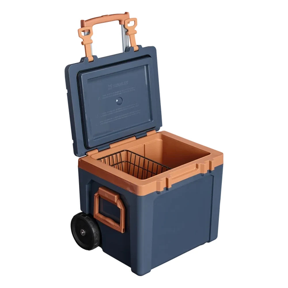 Stanley The Cold For Days Wheeled Outdoor Cooler 50QT in Twilight three-quarter open view on white background showing the orange interior with the black wire divider basket installed inside, telescoping handle extended at the top, and side handle with single large all-terrain wheel visible