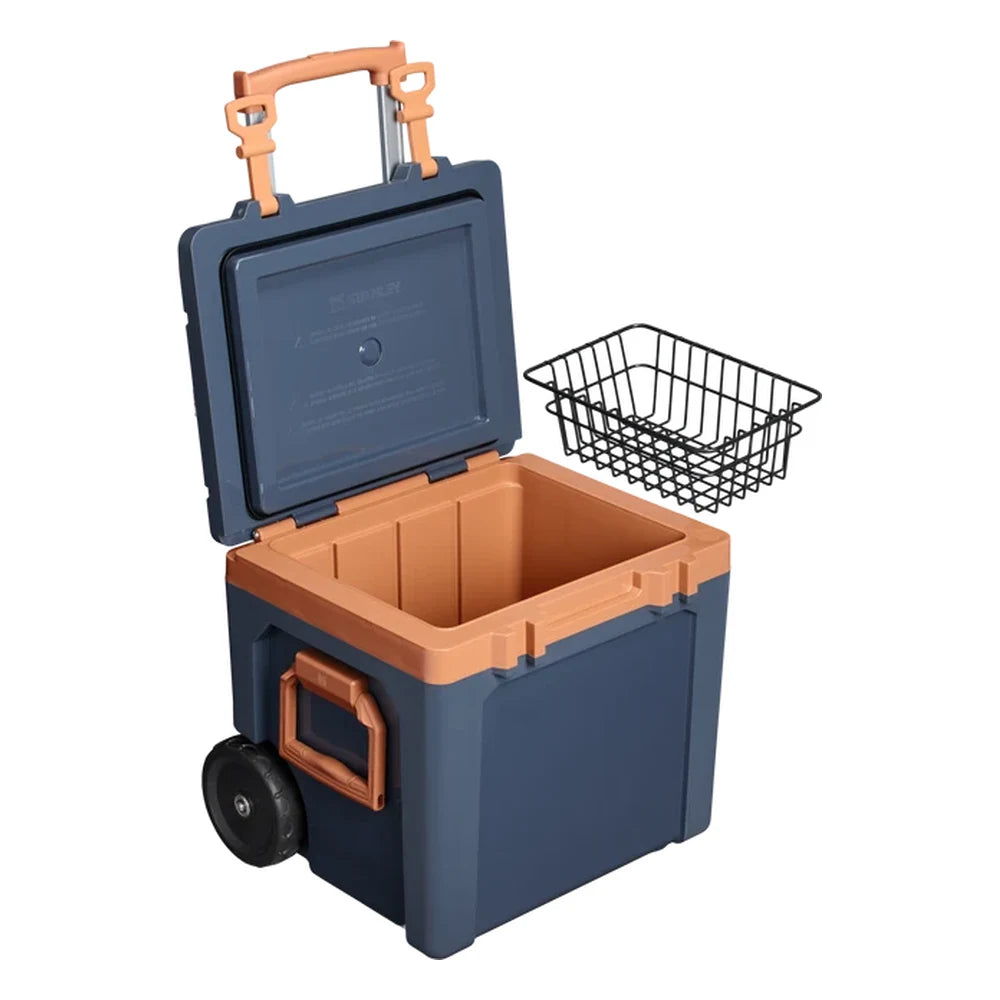 Stanley The Cold For Days Wheeled Outdoor Cooler 50QT in Twilight open view on white background with lid fully hinged back showing the orange interior, telescoping handle extended at the top, single large wheel visible, and the removable black wire basket accessory placed outside to the right