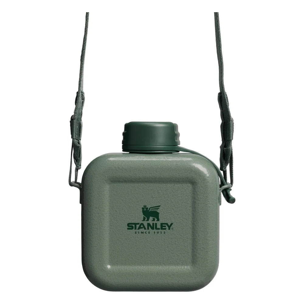 Stanley Next X Nature Canteen in Hammertone Green front view hanging from an adjustable nylon shoulder strap on white background, showing square hammertone green enamel body with Stanley Since 1913 winged bear logo, green screw-top cap with tether cord, and strap attachment points on both sides