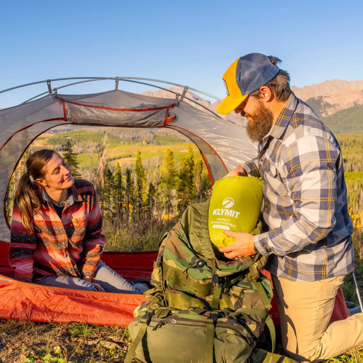 Hiker packing Klymit Static V Summit Double sleeping pad into backpack at campsite
