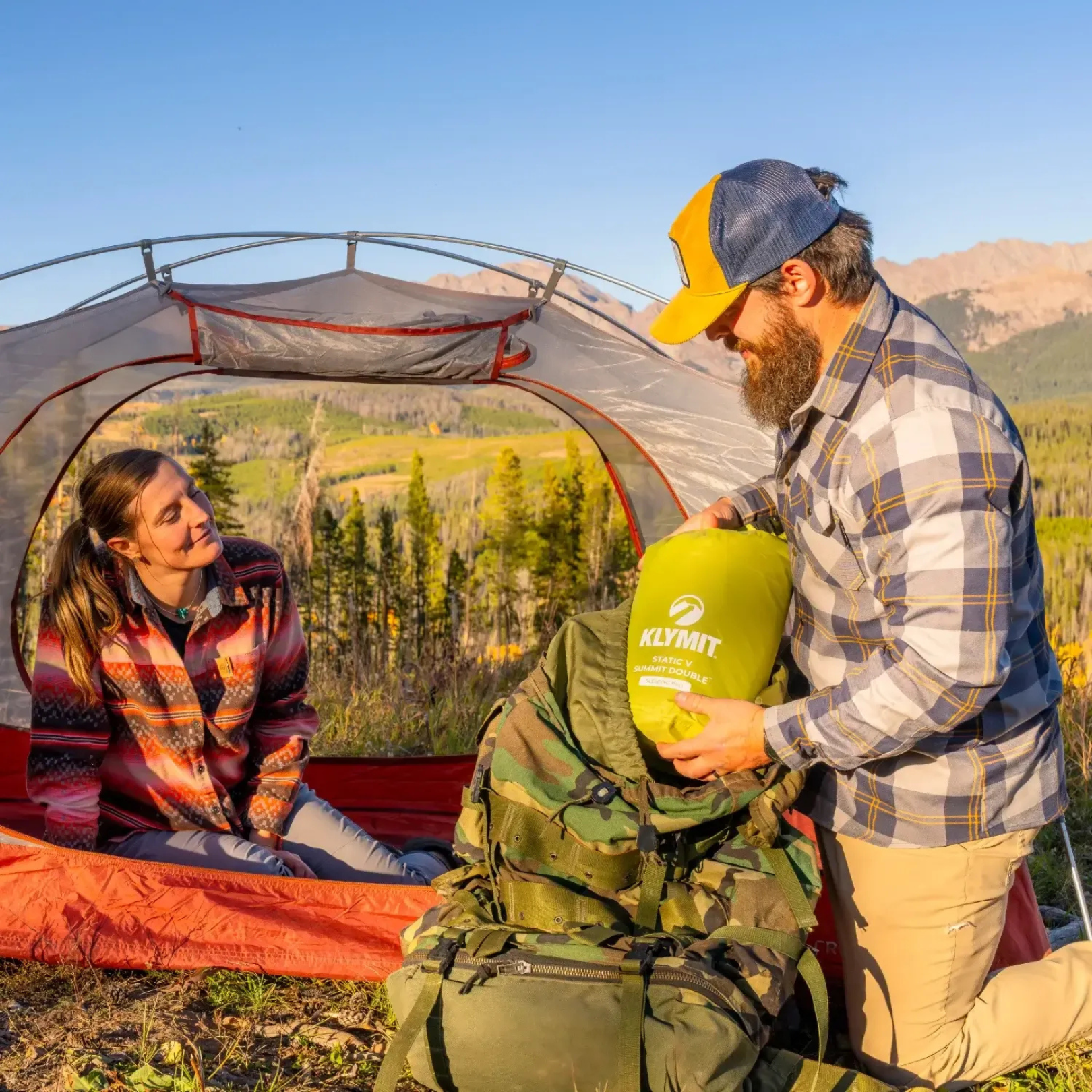 Hiker packing Klymit Static V Summit Double sleeping pad into backpack at campsite